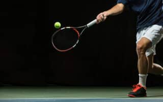 Close up photo of a man swinging a tennis racquet during a tennis match